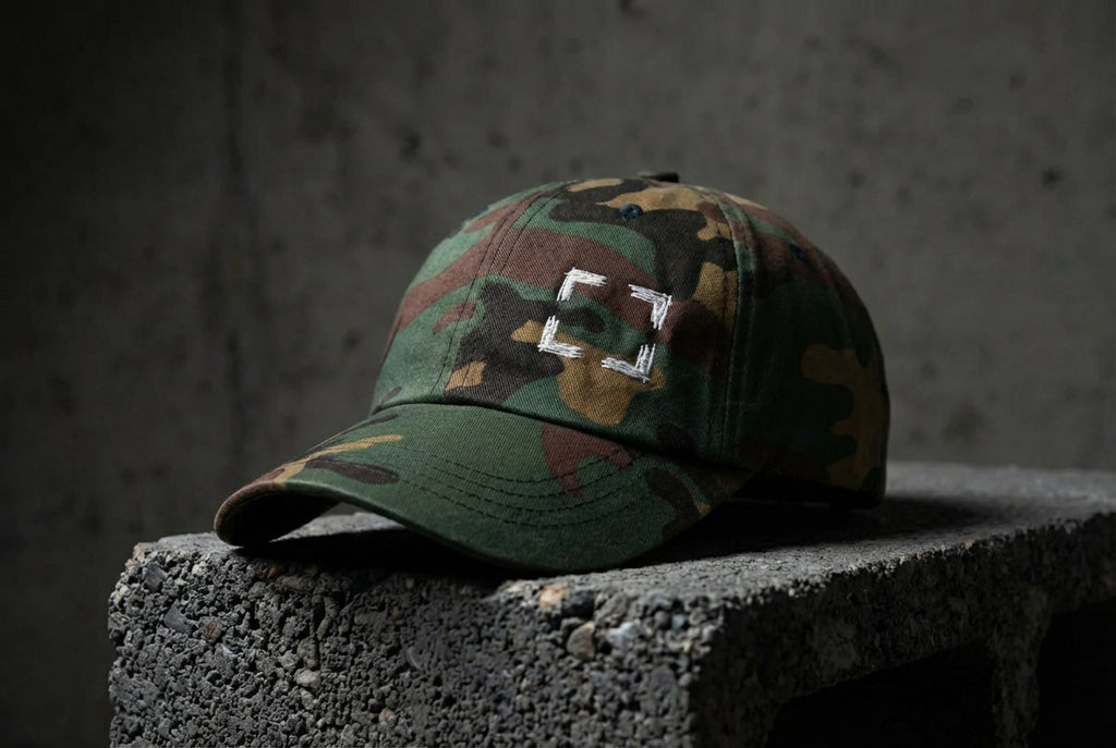 Green camo Cornerstone Hat with four light embroidered corner marks on concrete.