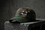 Green camo Cornerstone Hat with four light embroidered corner marks on concrete.