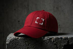 Cranberry Cornerstone Hat with four light embroidered corner marks on concrete.