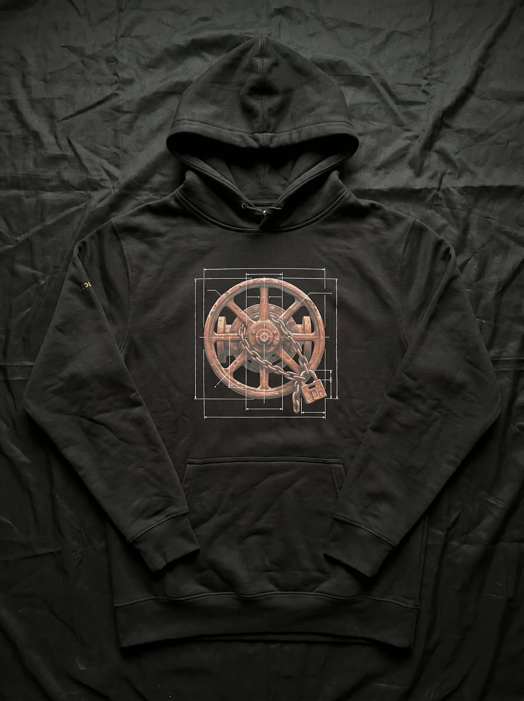 An isolated product mockup of the premium black graphic hoodie. The layout cleanly showcases the high-contrast white technical line-work, architectural blueprint grid lines, and the centered weathered wheel with its interlocking chain and padlock design against the dark fabric.