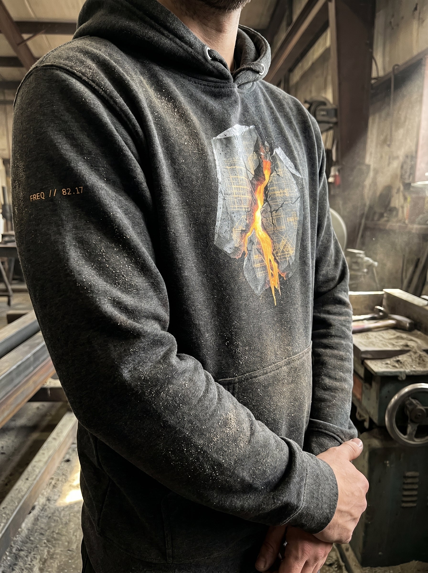 Side view of a model wearing the Charcoal Heather Transmission: Breach // Freq: 02.17 hoodie, highlighting the premium fabric texture and structural fit in an industrial workspace.
